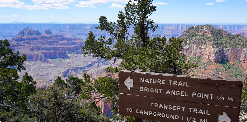 Grand Canyon trail sign with scenic layered rock formations and forest view